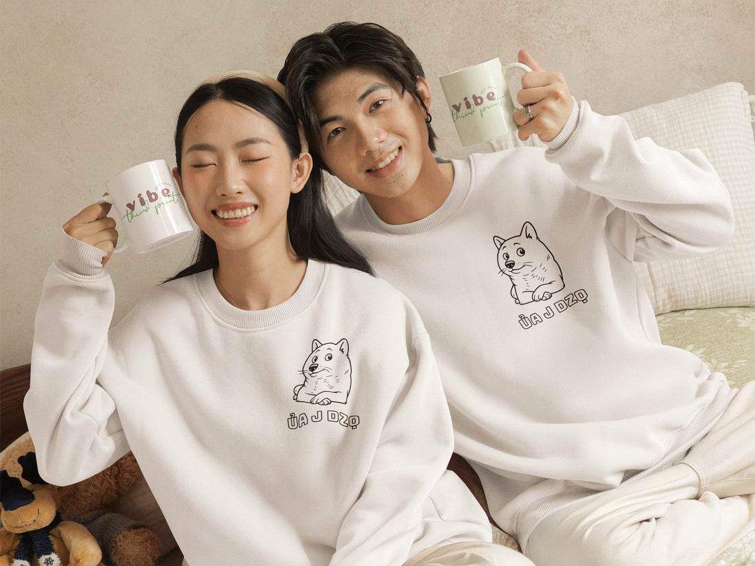 Smiling couple wearing matching white crewnecks with a cute dog illustration and the Vietnamese phrase “Ủa J Dzọ,” holding mugs with “Vibe Thread Print” logo. A cozy, minimalist outfit from a small online apparel brand for teens and young adults.