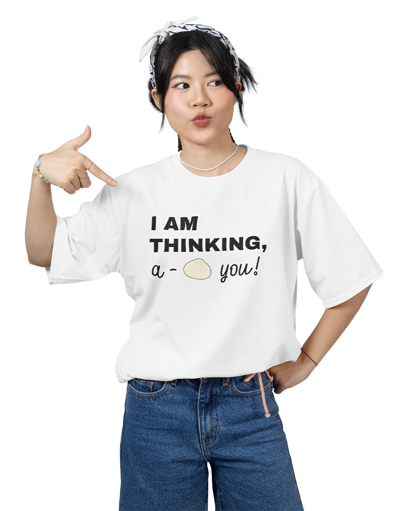 Young woman wearing a white graphic T-shirt with the funny phrase “I Am Thinking, A-Bao You” and a bao bun illustration. A playful, kawaii-style tee from a small online apparel shop specializing in cute, pun-inspired fashion for teens and young adults.