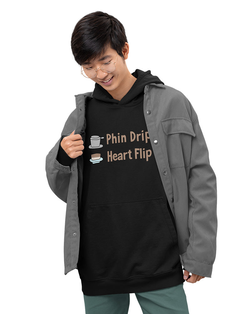 Young man smiling in a black hoodie with the text “Phin Drip Heart Flip” and cute Vietnamese coffee phin graphics. Cozy streetwear style from a small online apparel shop selling kawaii, pun-inspired designs for teens and young adults.