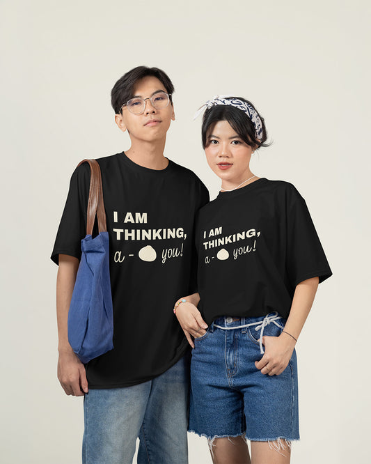Male and female models wearing matching black cute bao graphic tees with relaxed unisex fit for young adults.