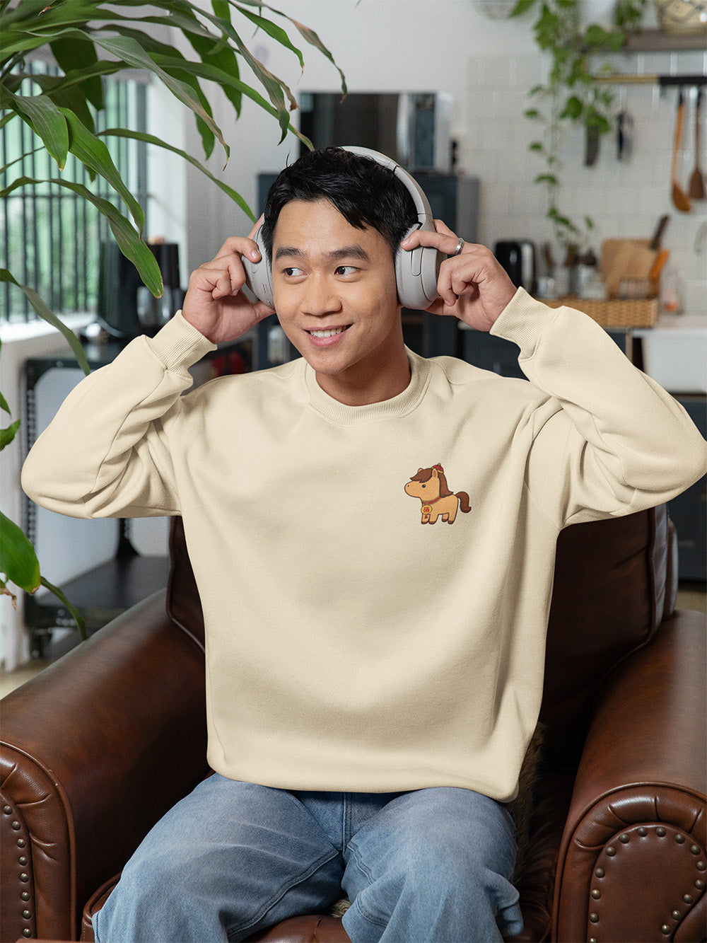 Smiling young man wearing a bone oversized crewneck sweatshirt with cute horse graphic, cozy kawaii streetwear for teens and young adults.