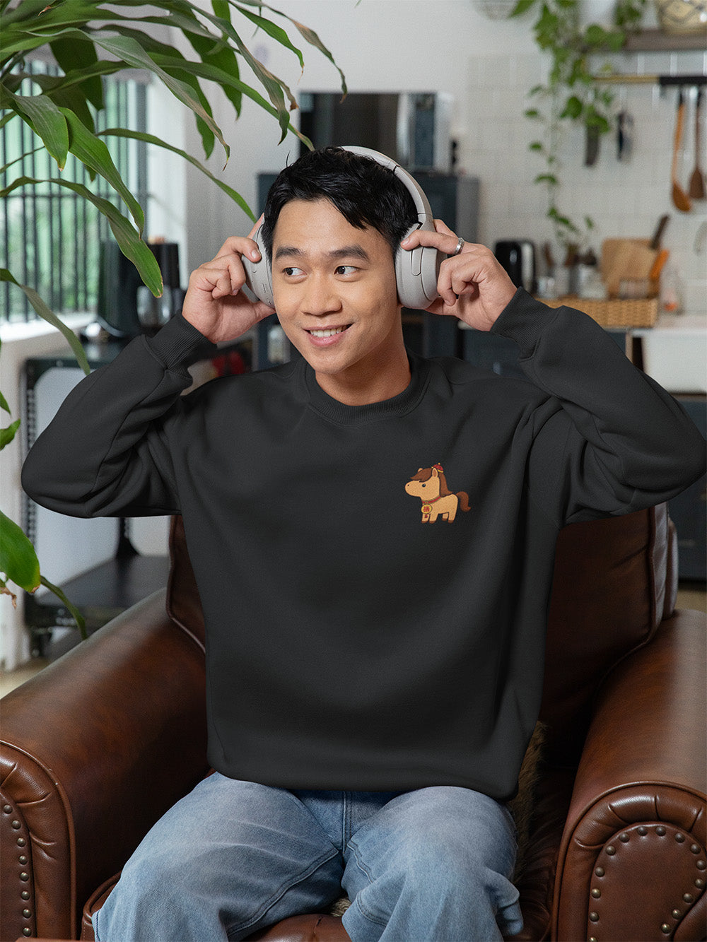 Young adult wearing black oversized crewneck sweatshirt with embroidered horse design, cozy modern streetwear for teens and young adults.