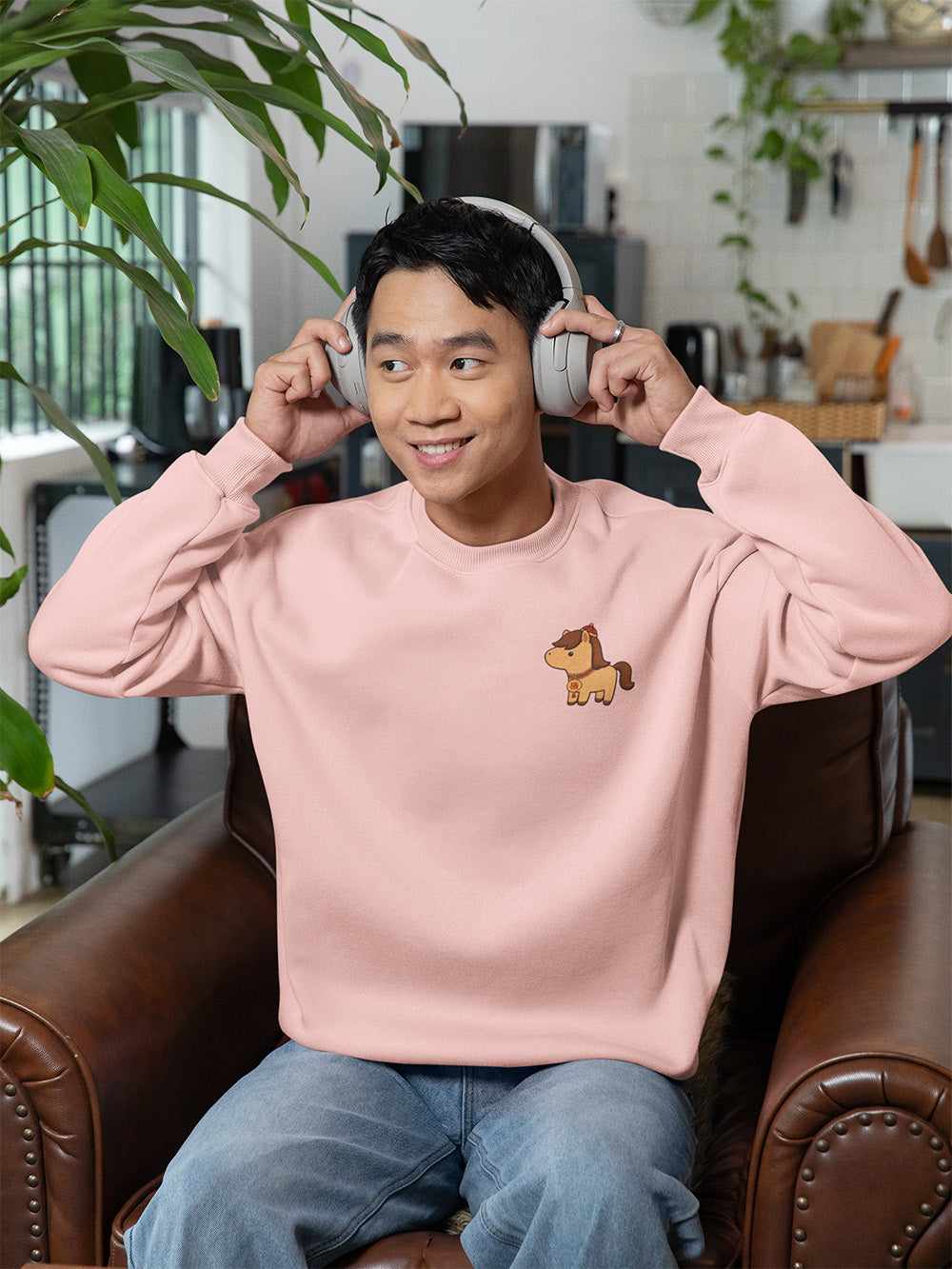 Young man in light pink oversized crewneck sweatshirt with cute horse embroidery, pastel kawaii fashion for cozy teen streetwear style.