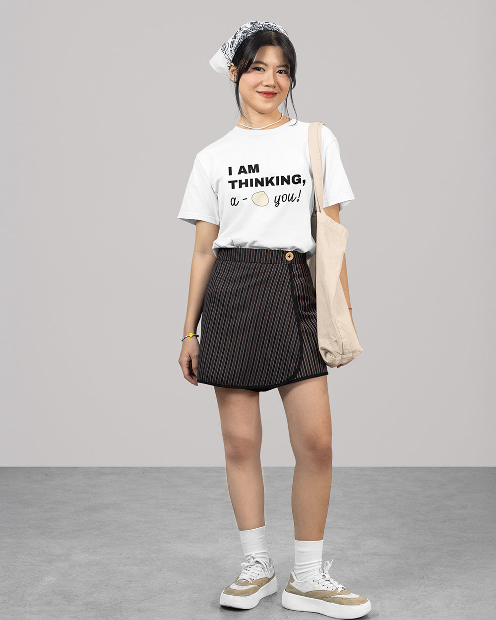 Full body female model wearing white cute bao graphic t-shirt with youthful casual outfit and tote bag styling.