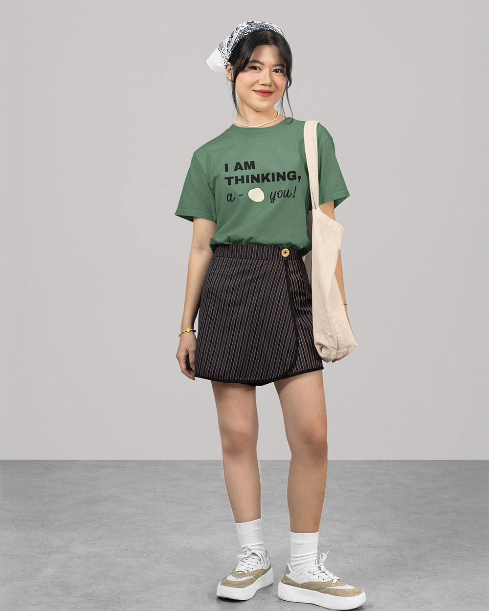 Full body female model wearing light green cute bao graphic t-shirt with youthful casual outfit and tote bag styling.