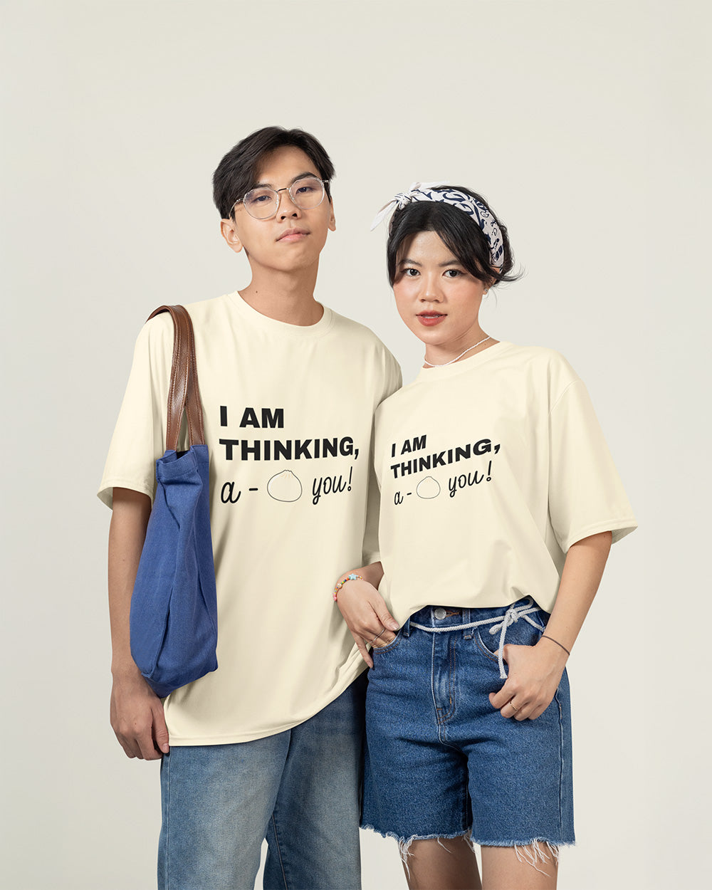 Male and female models wearing matching ivory cute bao bun graphic t-shirts with relaxed unisex fit style.