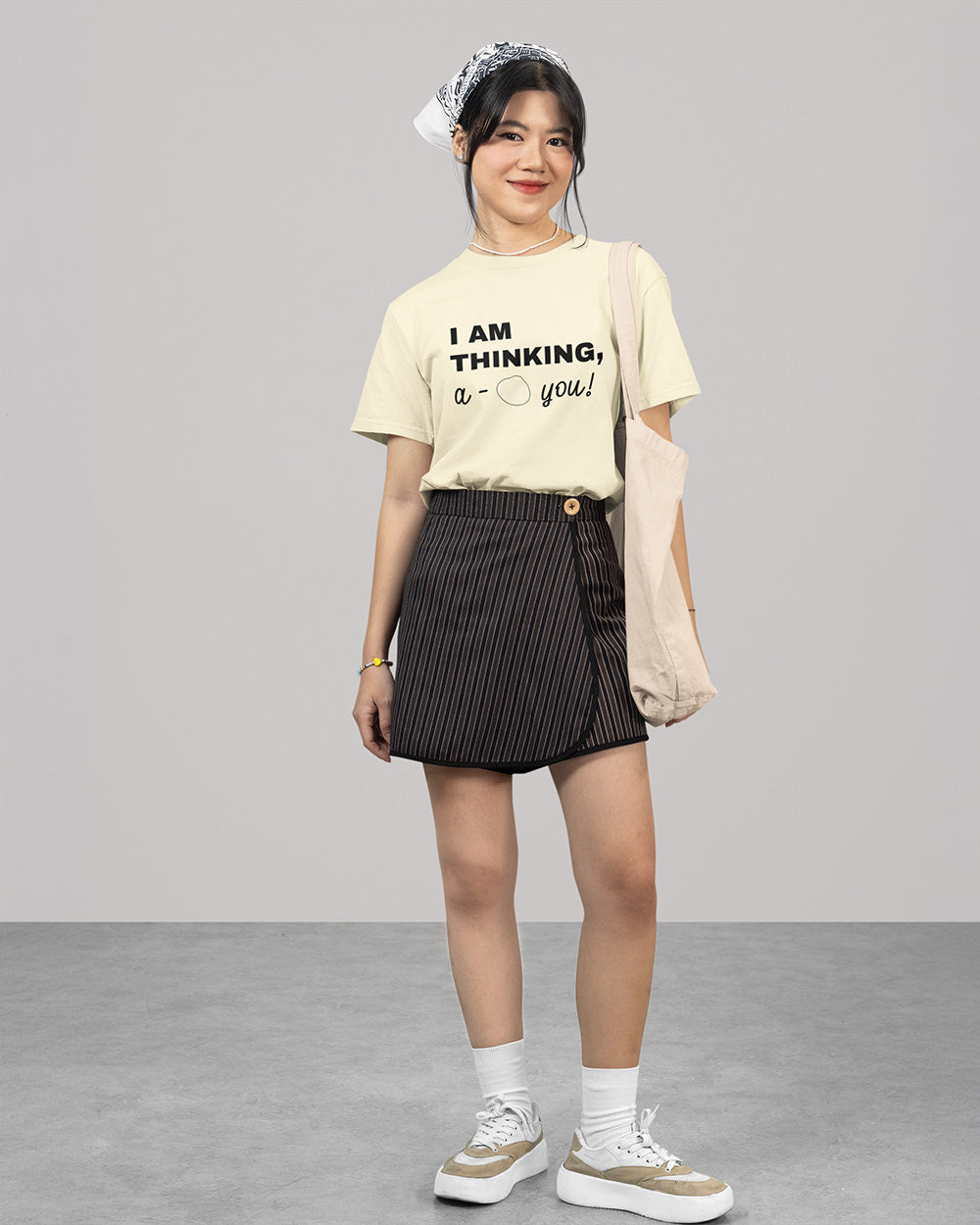 Full body female model wearing ivory cute bao graphic t-shirt with youthful casual outfit and tote bag styling.