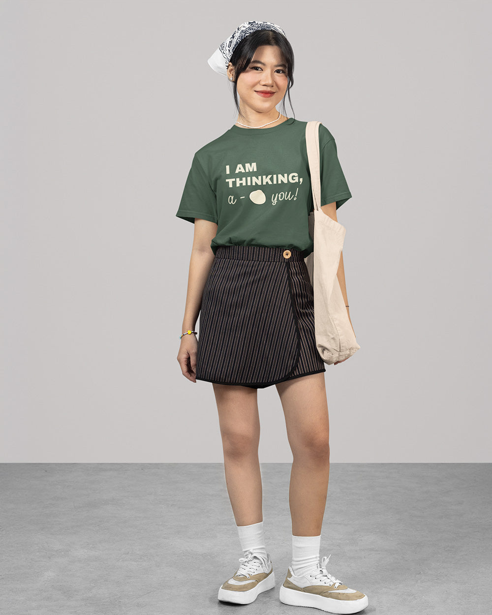 Full body female model wearing blue spruce cute bao graphic t-shirt with youthful casual outfit and tote bag styling.