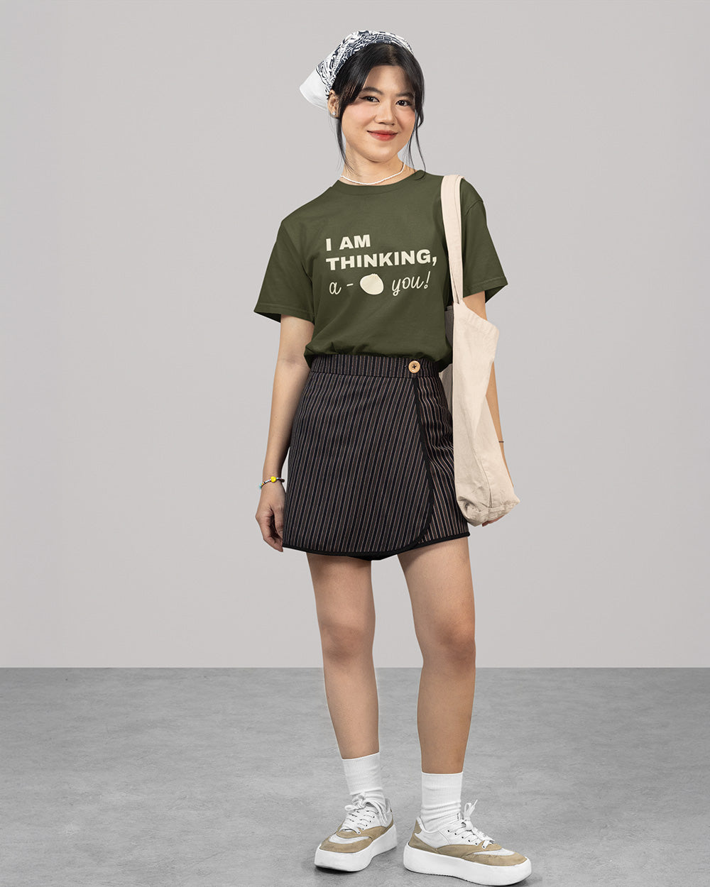 Full body female model wearing sage green cute bao graphic t-shirt with youthful casual outfit and tote bag styling.
