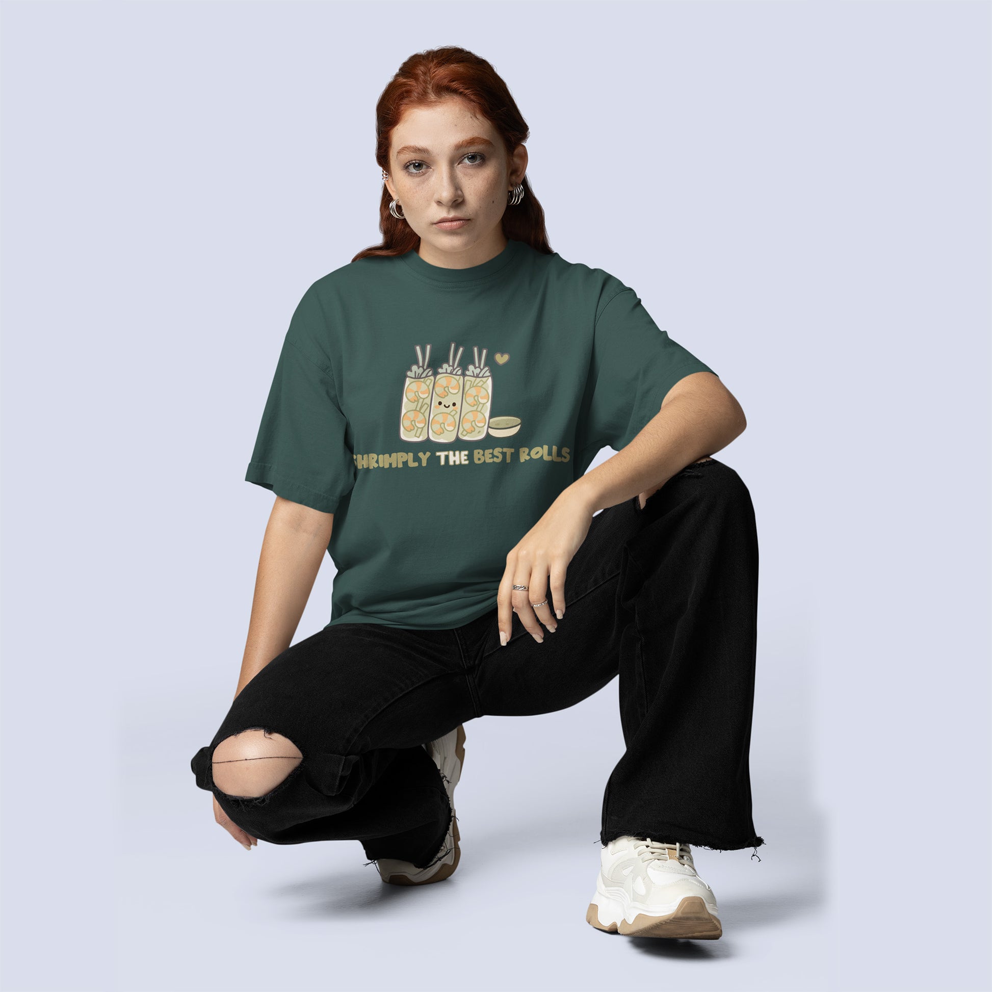 A woman wearing green, blue spruce T-shirt with cute shrimp spring roll graphic, dipping sauce, heart, and text “SHRIMPLY THE BEST ROLLS.”