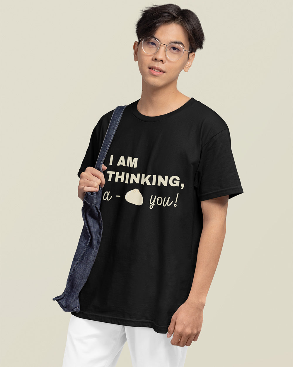 Male model holding denim tote bag while wearing black “I Am Thinking, a Bao You!” T-shirt from Vibe Thread Print. Soft cotton graphic tee for food lovers and cozy outfit enthusiasts.