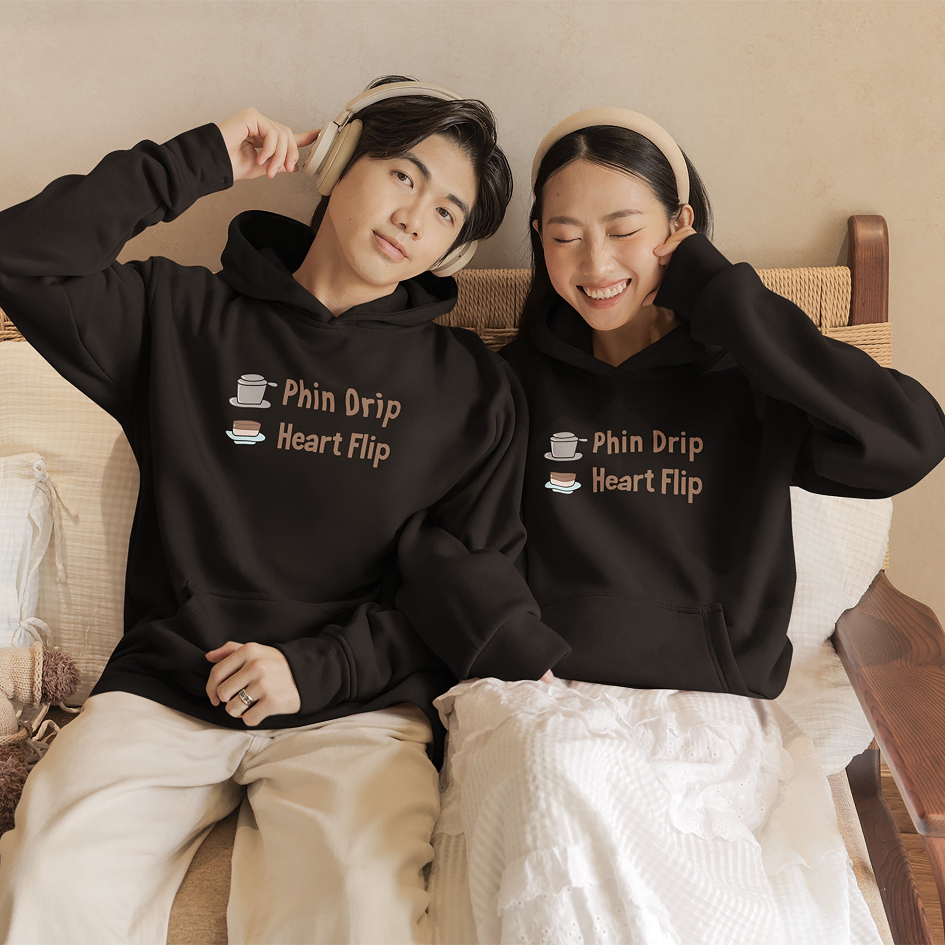 Two people wearing matching black hoodies with text, sitting on a couch.