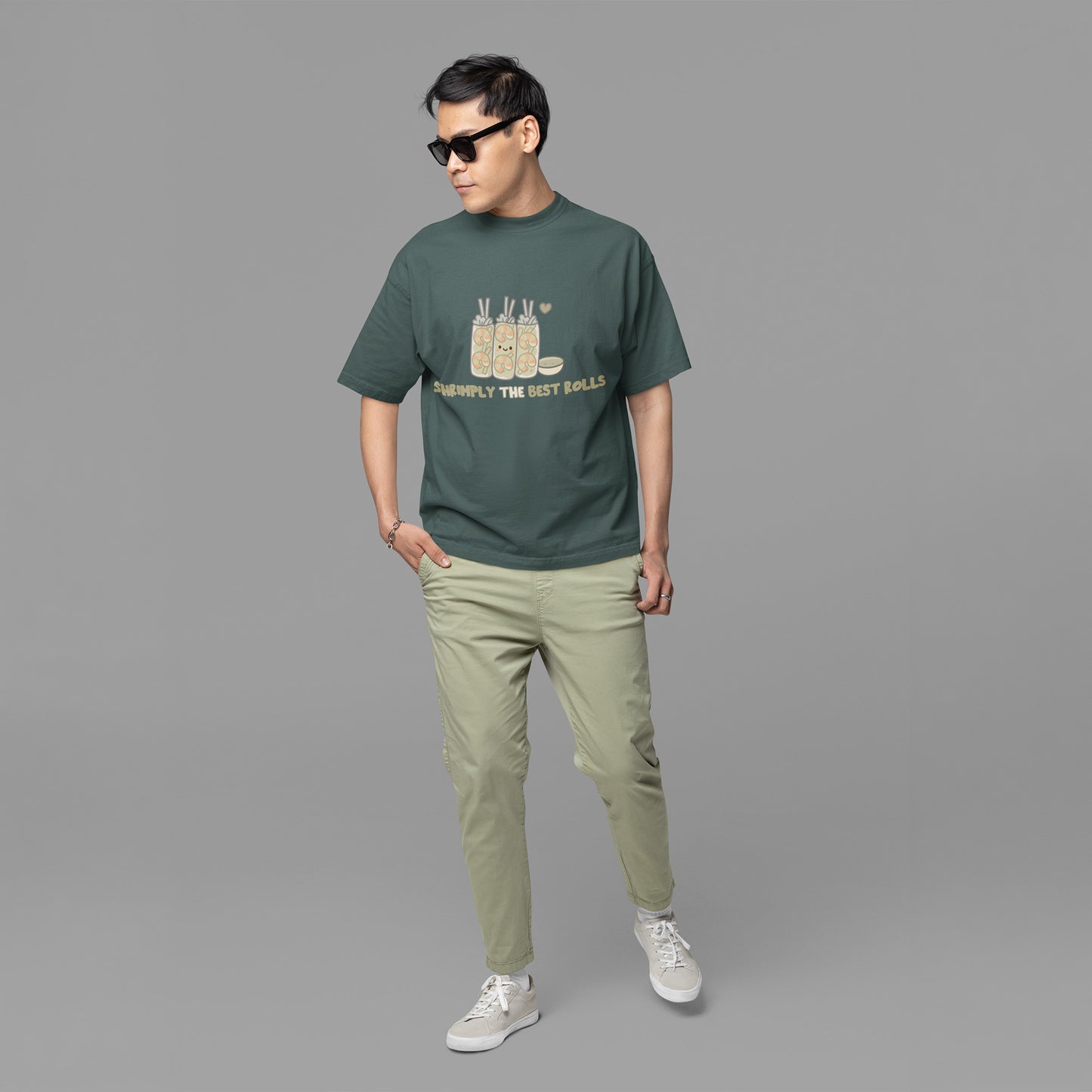 Young man wearing a blue spruce kawaii graphic t-shirt featuring cute spring rolls with the phrase “Shrimply the Best Rolls,” styled with casual pants and sneakers.