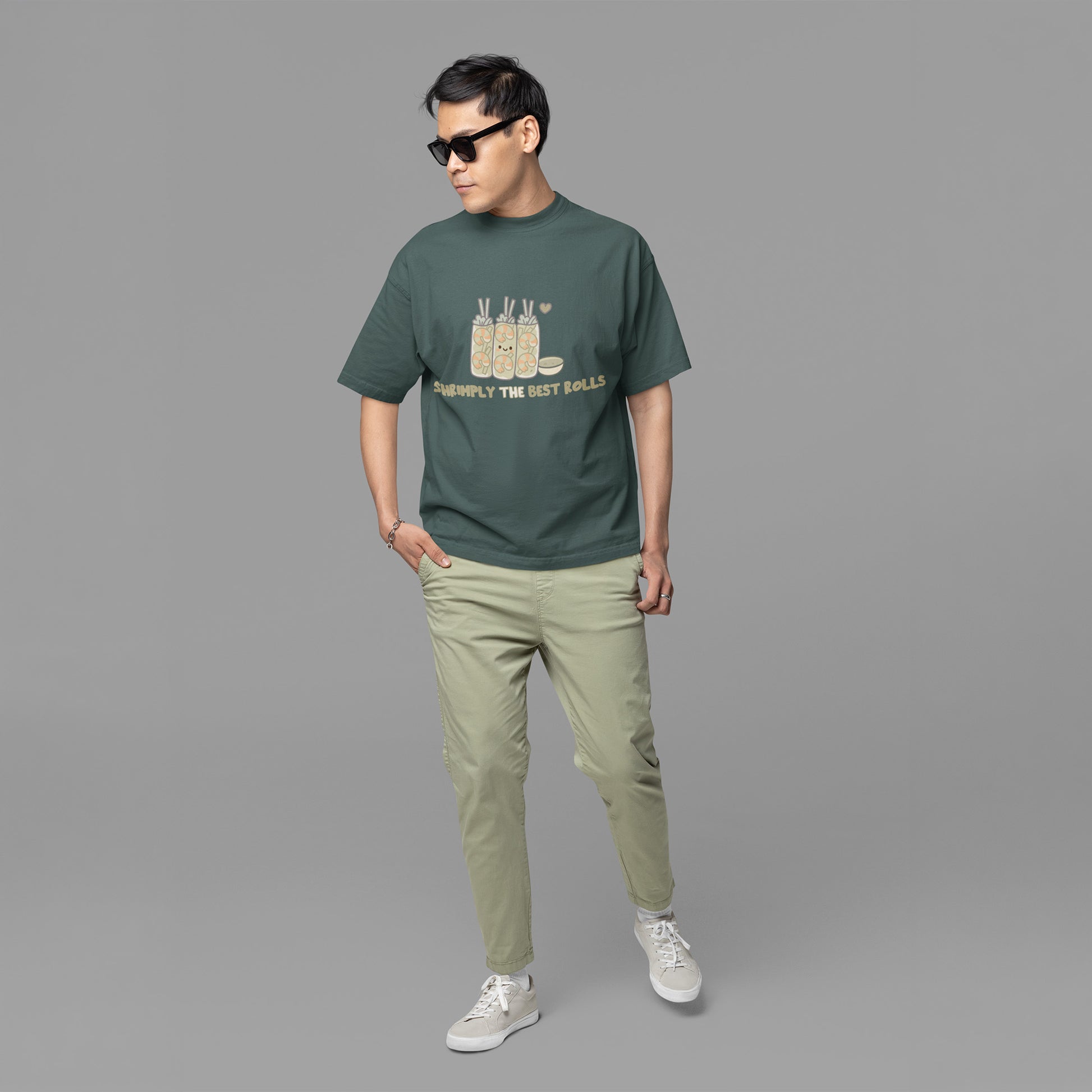 Young man wearing a blue spruce kawaii graphic t-shirt featuring cute spring rolls with the phrase “Shrimply the Best Rolls,” styled with casual pants and sneakers.