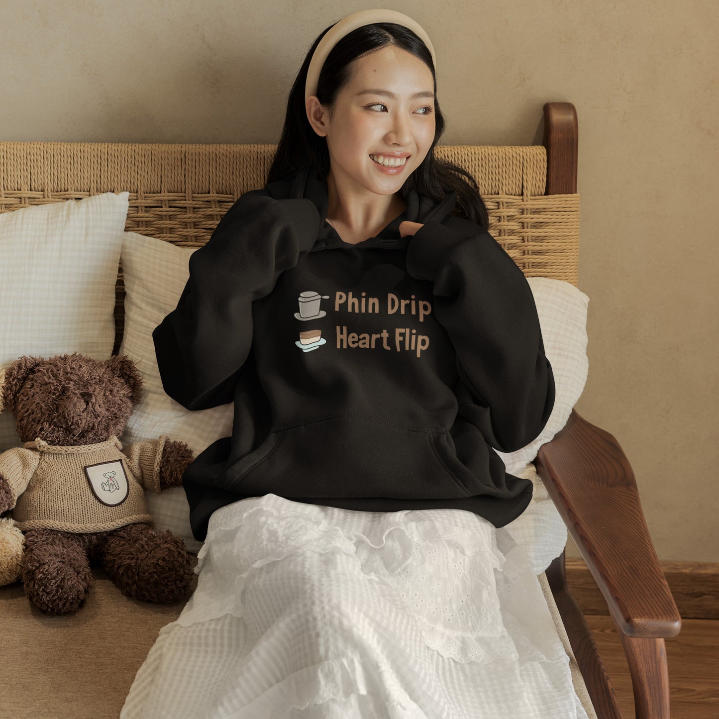 Woman wearing a black hoodie with text, sitting on a couch with a teddy bear.