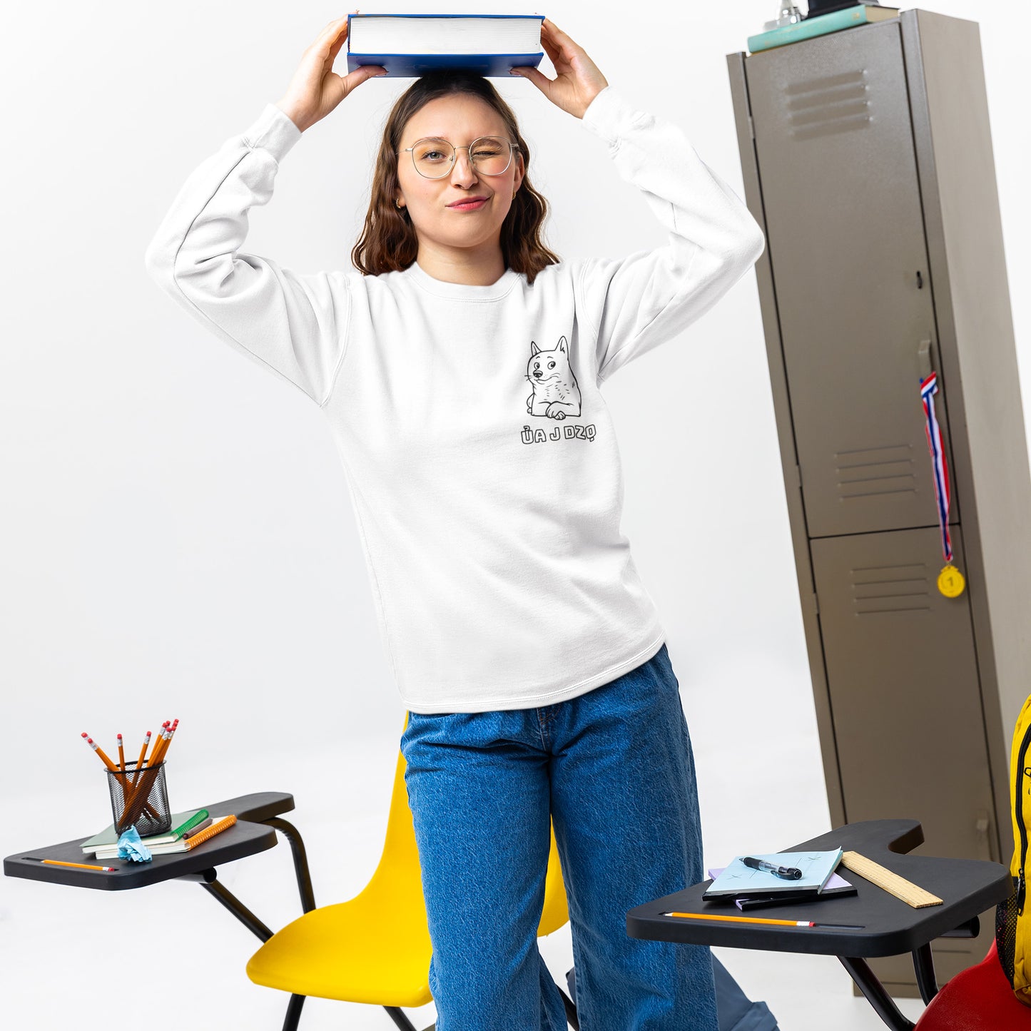 A girl wearing a white sweatshirt with a dog graphic, standing next to a locker with a yellow chair and small tables in the foreground.