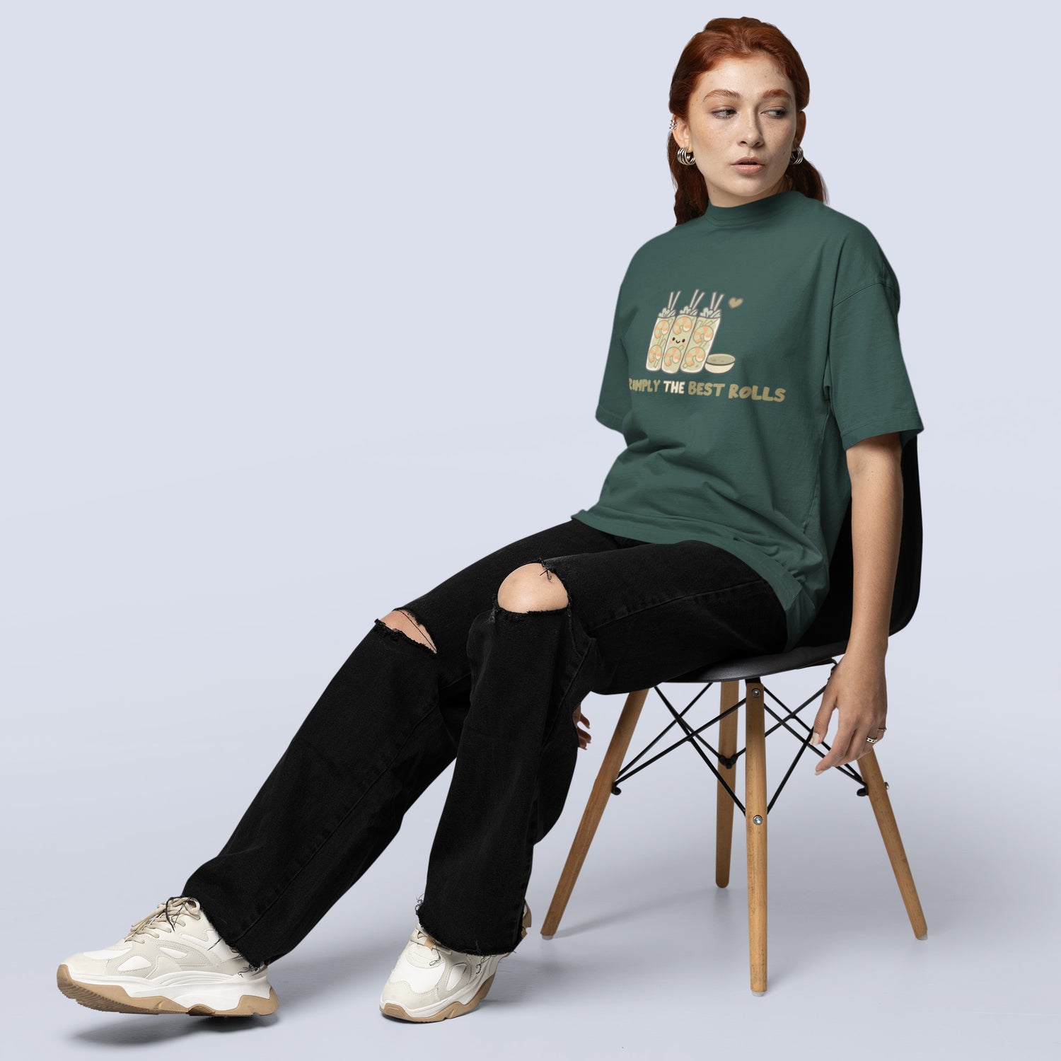 A woman wearing a blue spruce t-shirt with text, sitting on a chair against a light gray background.